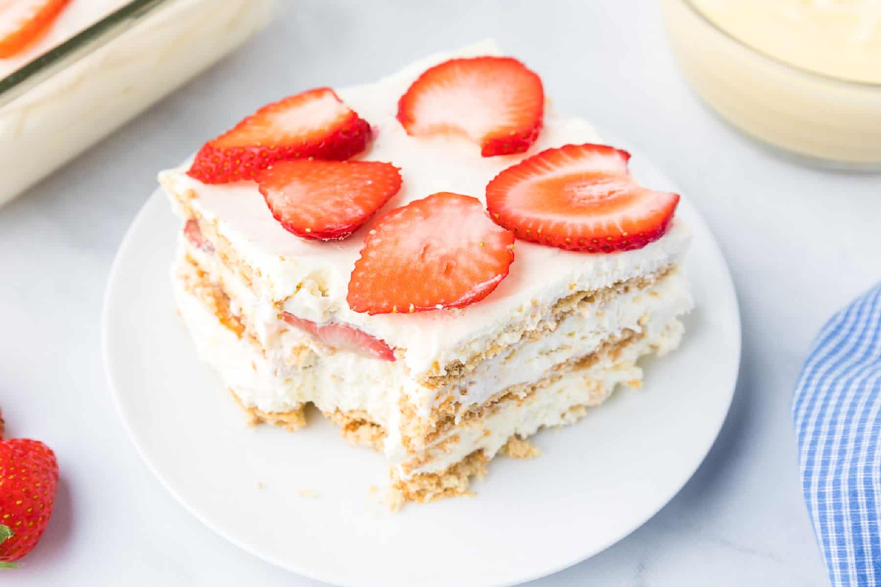 A slice of strawberry cream cheese icebox cake, a layered dessert with whipped cream, graham crackers, and fresh strawberry slices.