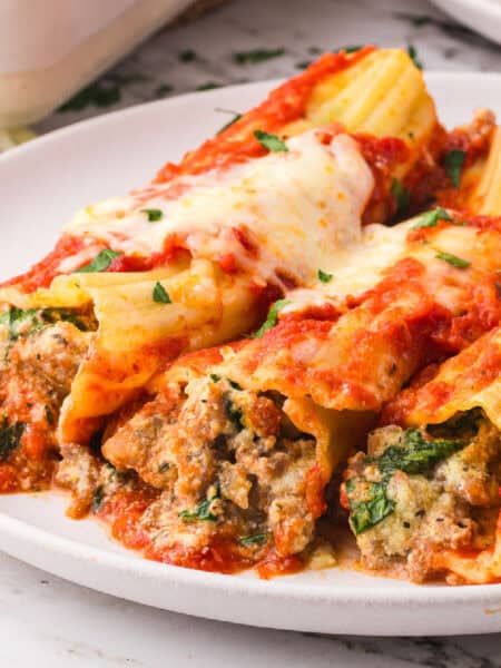 Three stuffed manicotti pasta shells stuffed with sausage filling and topped with melted cheese and tomato sauce are served on a white plate.