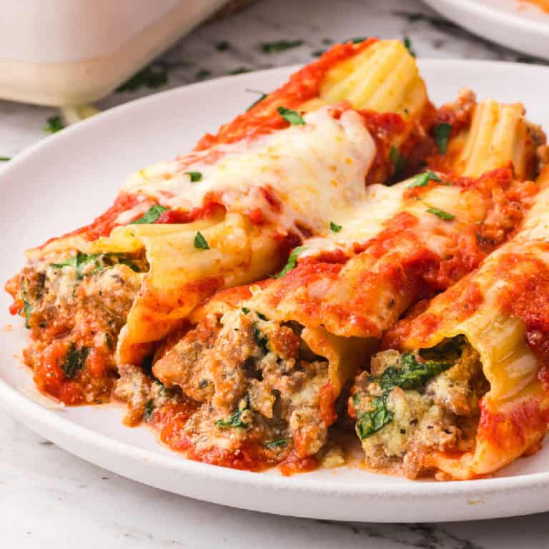 Three stuffed manicotti pasta shells stuffed with sausage filling and topped with melted cheese and tomato sauce are served on a white plate.