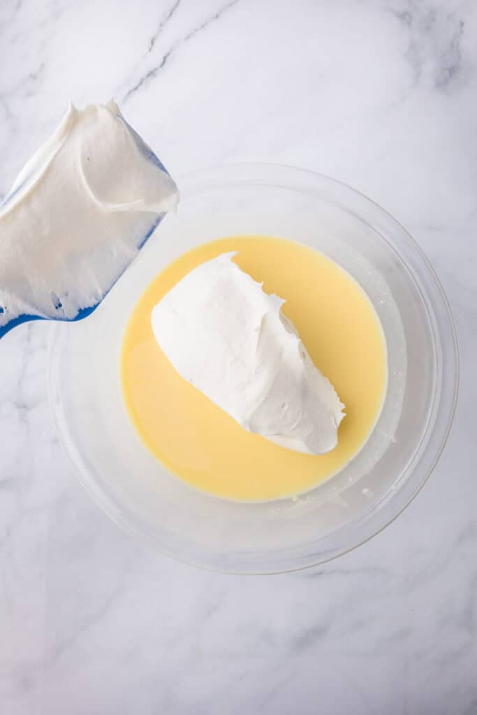 Cool Whip being folded into instant cheesecake pudding for no bake strawberry chocolate eclair cake.