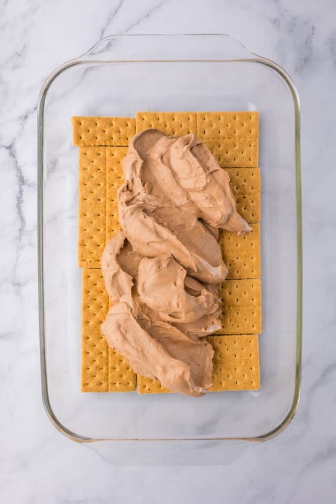 A glass baking dish with a layer of whole graham crackers, topped with a layer of chocolate pudding mixture for strawberry chocolate eclair cake.