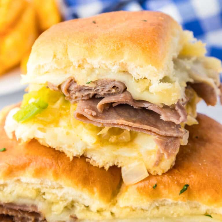A close-up of three philly cheesesteak sliders with melted cheese, chopped green onions, and onions on Hawaiian rolls.