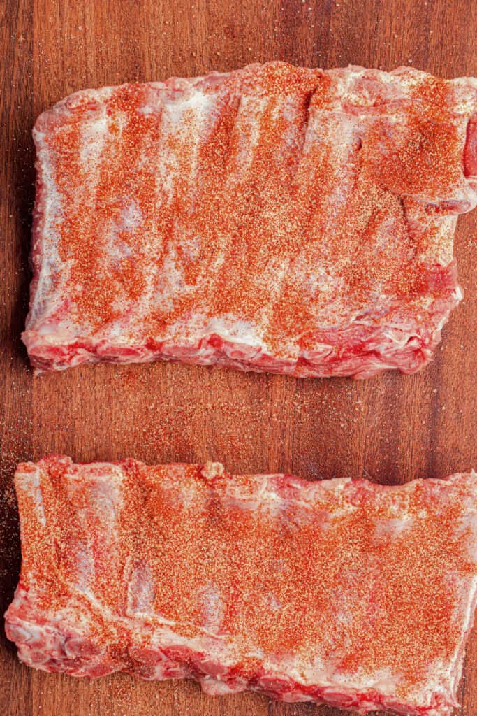 Two raw racks of pork ribs coated with dry seasoning rub on a cutting board for slow cooker garlic honey ribs.