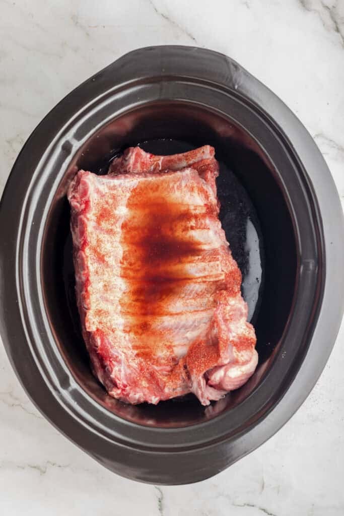 Raw pork ribs sprinkled with seasoning and topped with soy sauce for slow cooker garlic honey ribs.