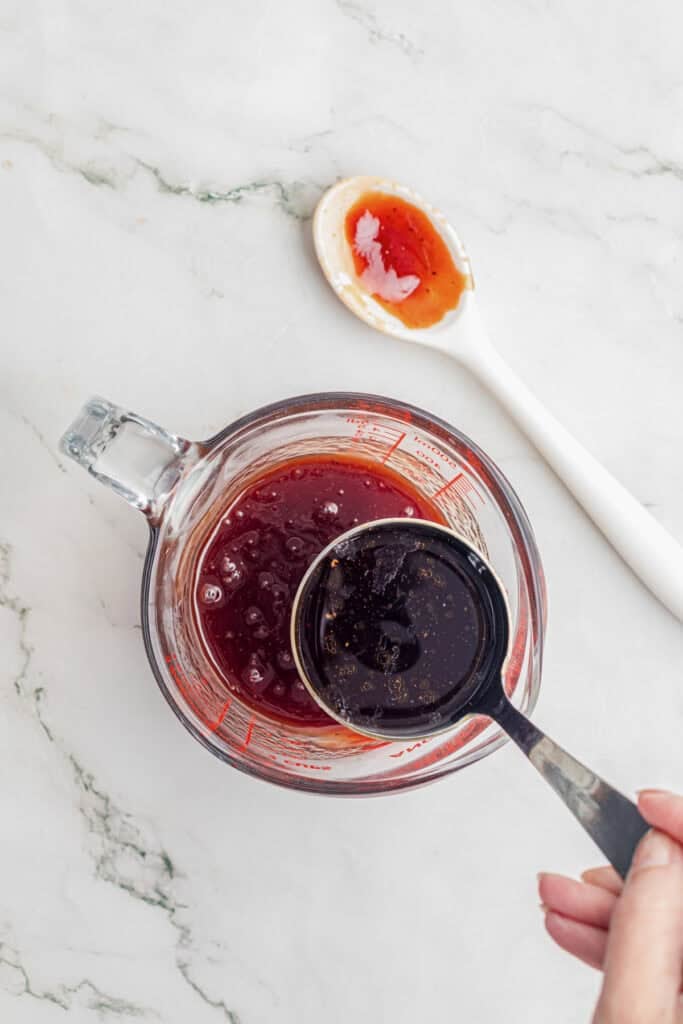 A hand holds a measuring cup with drippings from the slow cooker mixing into the bbq sauce mixture for slow cooker garlic honey ribs.
