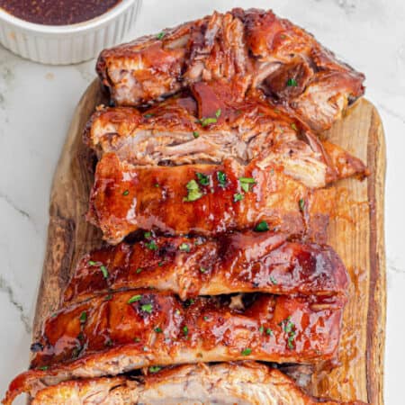 A wooden cutting board topped with glazed, cooked slow cooker garlic honey pork ribs sliced into portions.