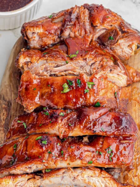 A wooden cutting board topped with glazed, cooked slow cooker garlic honey pork ribs sliced into portions.