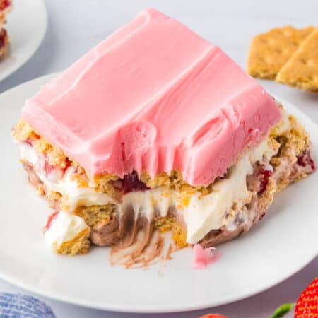 A close up os a slice of no bake strawberry chocolate eclair cake on a plate with a bite taken from the slide.