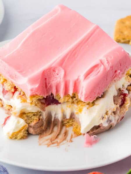 A close up os a slice of no bake strawberry chocolate eclair cake on a plate with a bite taken from the slide.