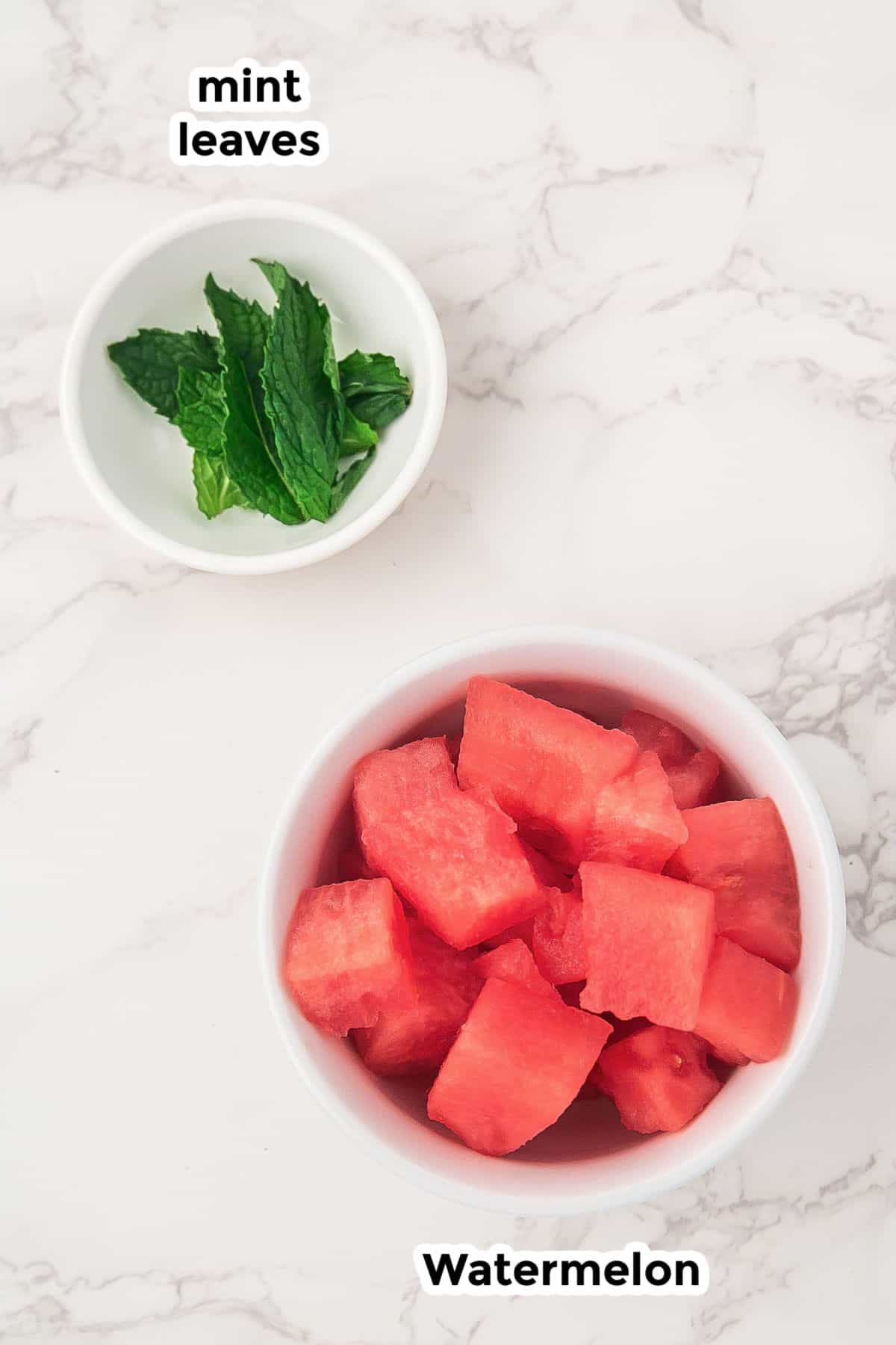 A bowl of cubed watermelon and a small bowl of fresh mint leaves for watermelon frozen dog treats.
