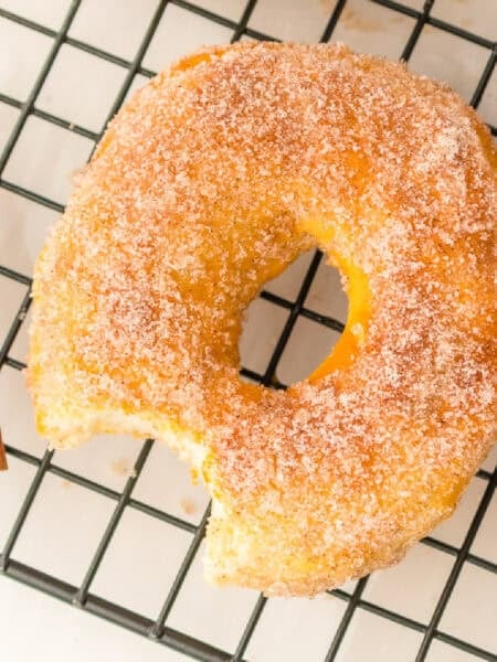 A cinnamon sugar air fryer biscuit donut with a bite taken out sits on a cooling rack.