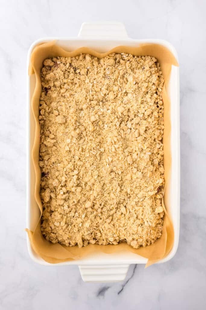 A rectangular white baking dish filled with cherry pie bars toped with a crumble topping before baking.