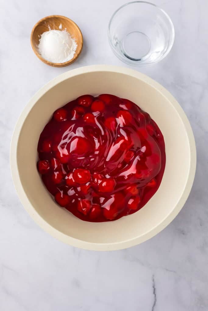 A bowl of cherry pie filling with cornstarch and water nearby.