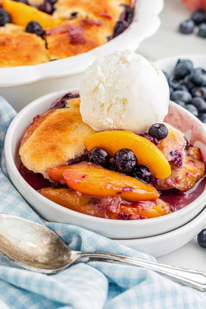 A serving of peach and blueberry cobbler topped with a scoop of vanilla ice cream on a table.