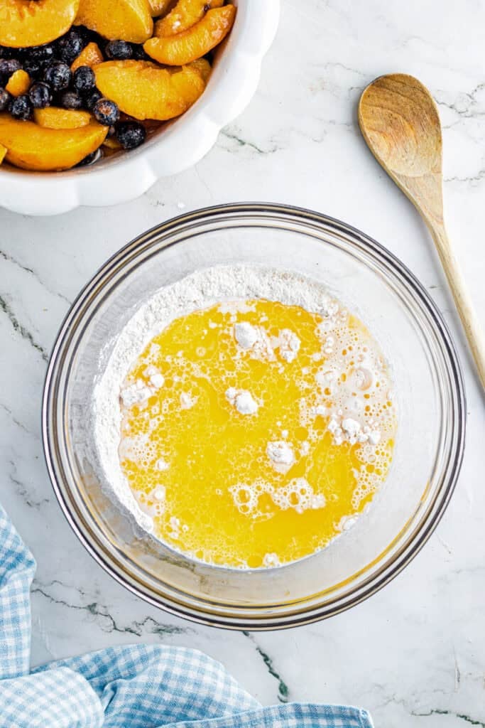 A glass bowl with melted butter and flour mixture to make the biscuit topping for peach blueberry cobbler.