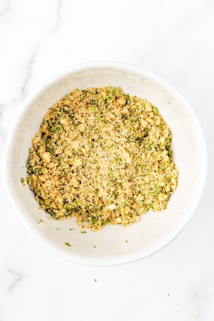 A white bowl filled with a mixture of brown sugar, herbs, and seasonings for the rub for pork loin wrapped in bacon.