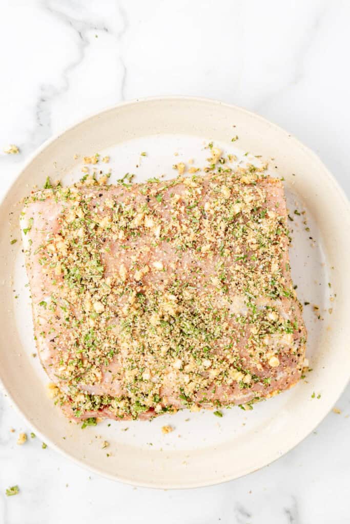 Raw pork loin coated with a mixture of herbs and breadcrumbs for pork loin wrapped in bacon.