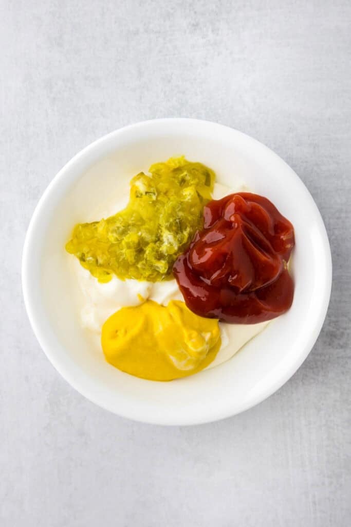 A white bowl containing mayonnaise, yellow mustard, ketchup, and pickle relish for a burger sauce for smash burger tacos.
