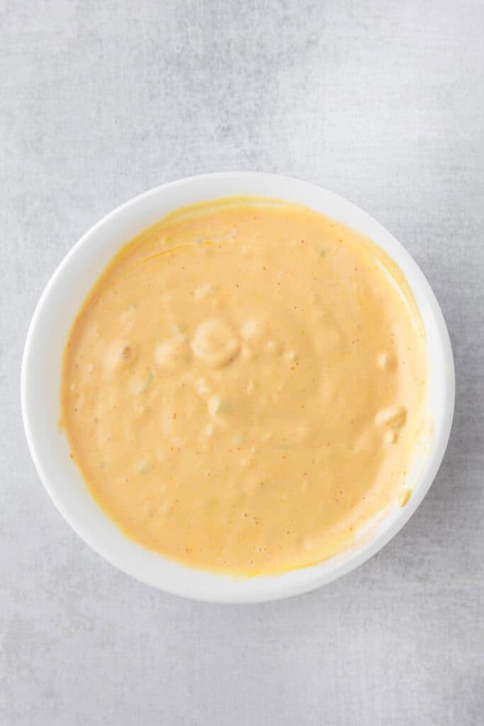 A white bowl filled with creamy orange burger sauce after mixing for smash burger tacos.