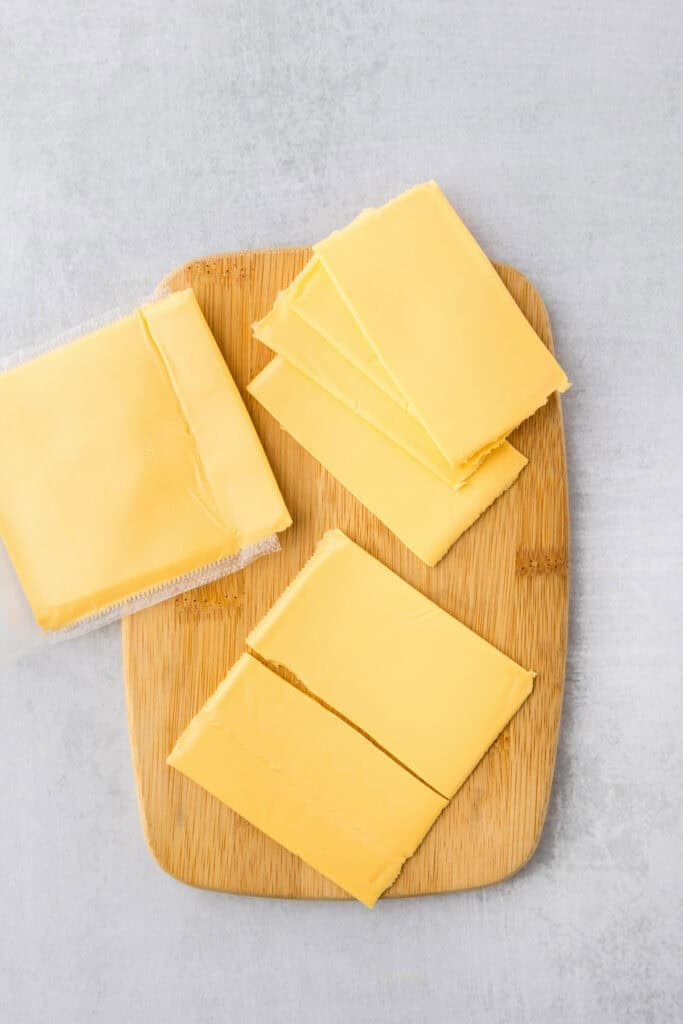 Several slices of American cheese, some wrapped and some unwrapped for smash burger tacos.