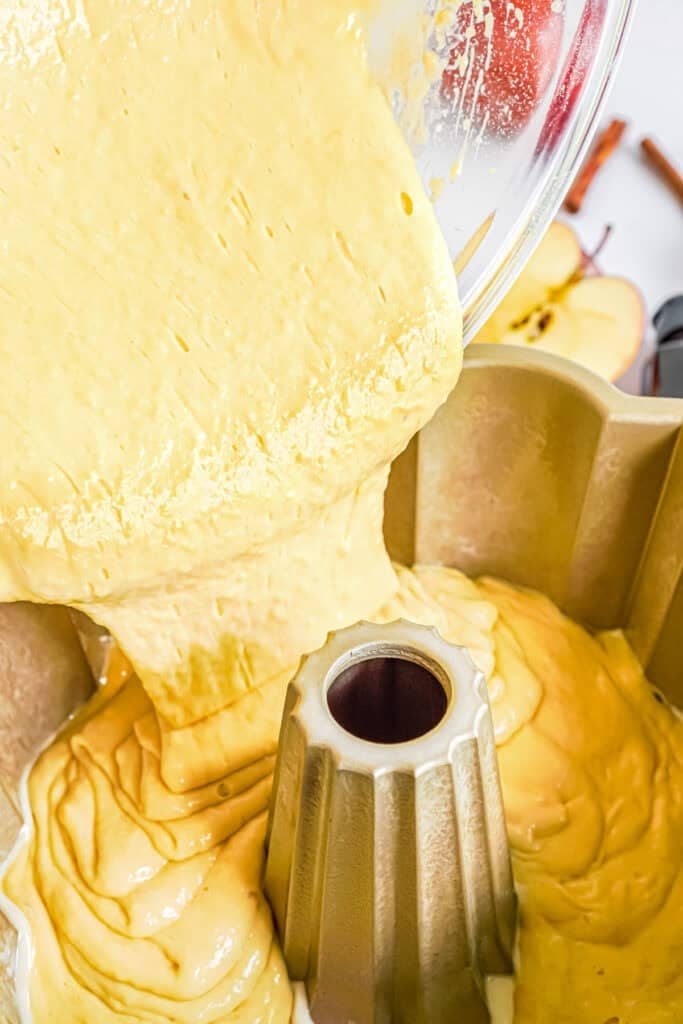 Apple cider donut cake batter being poured from a bowl into a greased bundt cake pan.