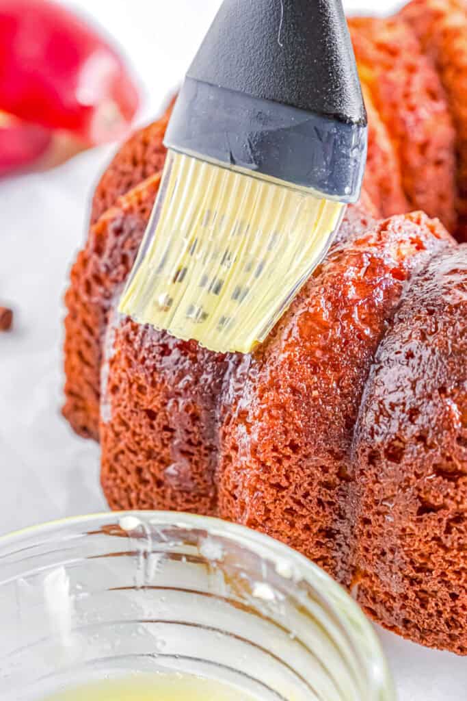 A pastry brush applies melted butter to an apple cider donut cake.