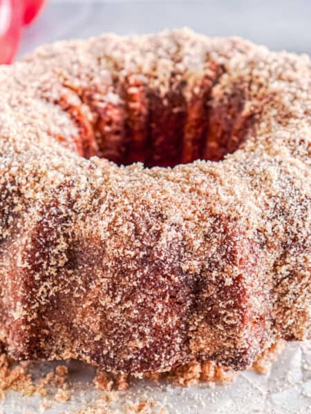 Apple cider donut cake coated with a layer of cinnamon sugar on parchement paper.