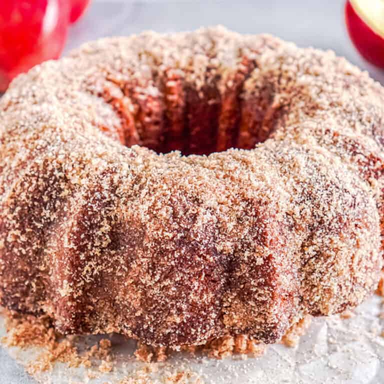 Apple cider donut cake coated with a layer of cinnamon sugar on parchement paper.