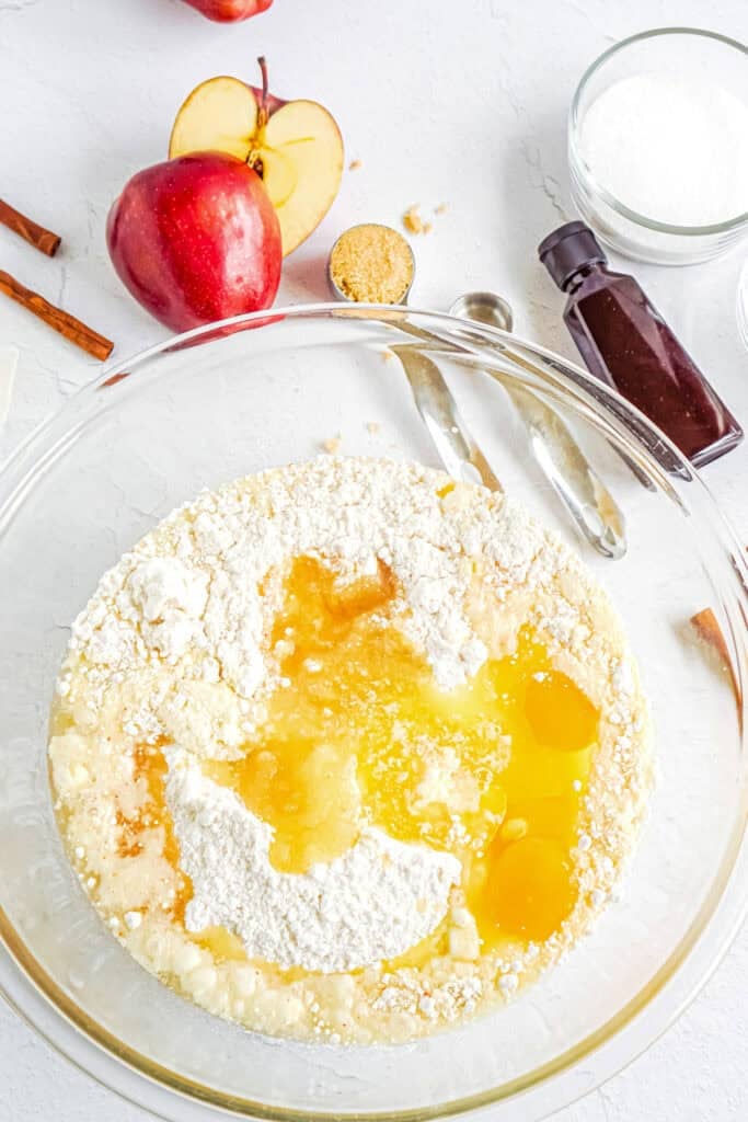 Glass bowl with cake mix, sugar, eggs, and applesauce being mixed ofr an apple cider donut cake.
