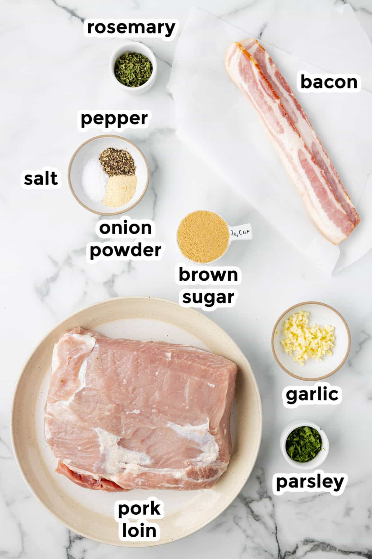 Ingredients for a pork lon wrapped in bacon recipe on a counter with text labels.