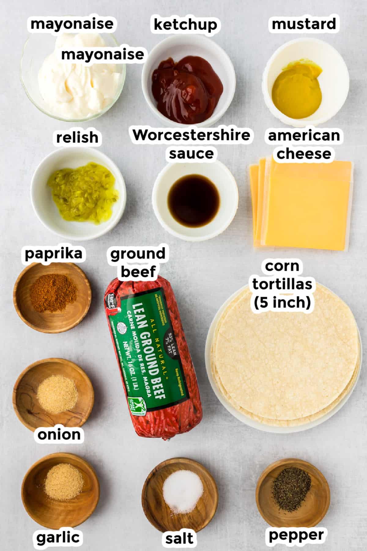 Assorted ingredients for smash burger tacos, including ground beef, cheese, corn tortillas, sauces, spices, relish, and seasonings.