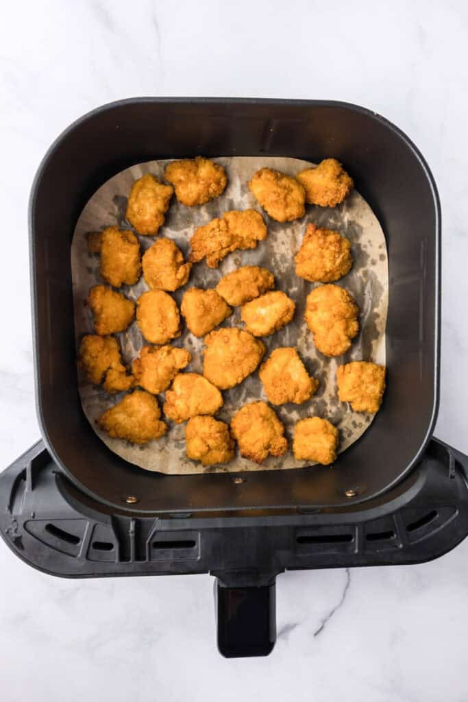 Golden brown cooked chicken nuggets on a parchment liner in an air fryer basket for chicken parmesan sliders.