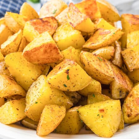 A plate of golden roasted crispy yellow potatoes seasoned with herbs and spices.