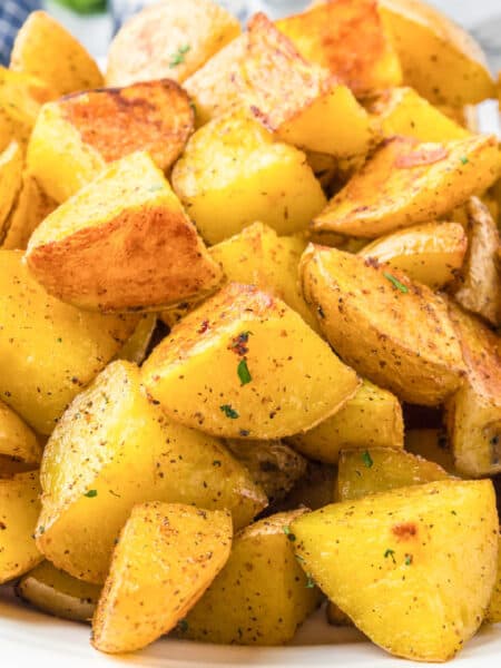 A plate of golden roasted crispy yellow potatoes seasoned with herbs and spices.