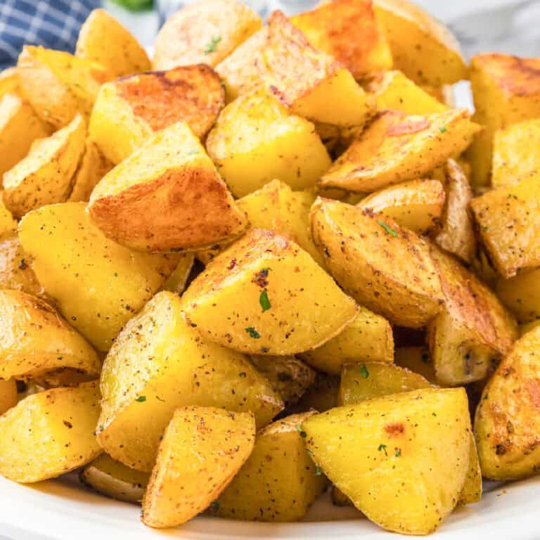 A plate of golden roasted crispy yellow potatoes seasoned with herbs and spices.