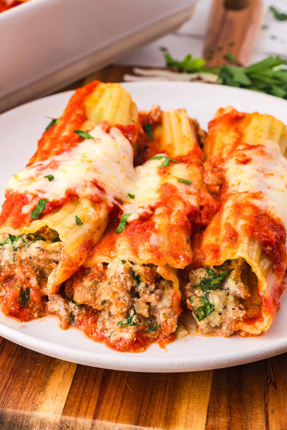 Three baked manicotti pasta shells stuffed with sausage, cheese, and spinach, topped with tomato sauce and melted cheese, served on a white plate.
