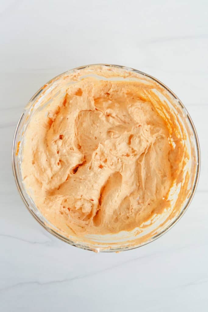 A glass bowl filled with a smooth, light orange creamy pumpkin pie dip right after mixing.