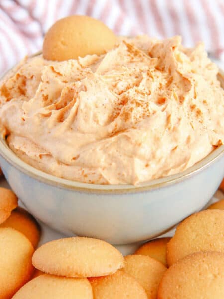 Finished close up view of pumpkin pie dip in a serving bowl surrounded by vanilla wafers with one cookie in the dip.