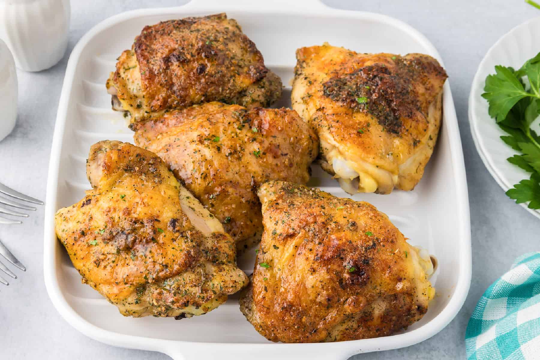 Five seasoned, baked crispy ranch chicken thighs on white rectangular dish being served.