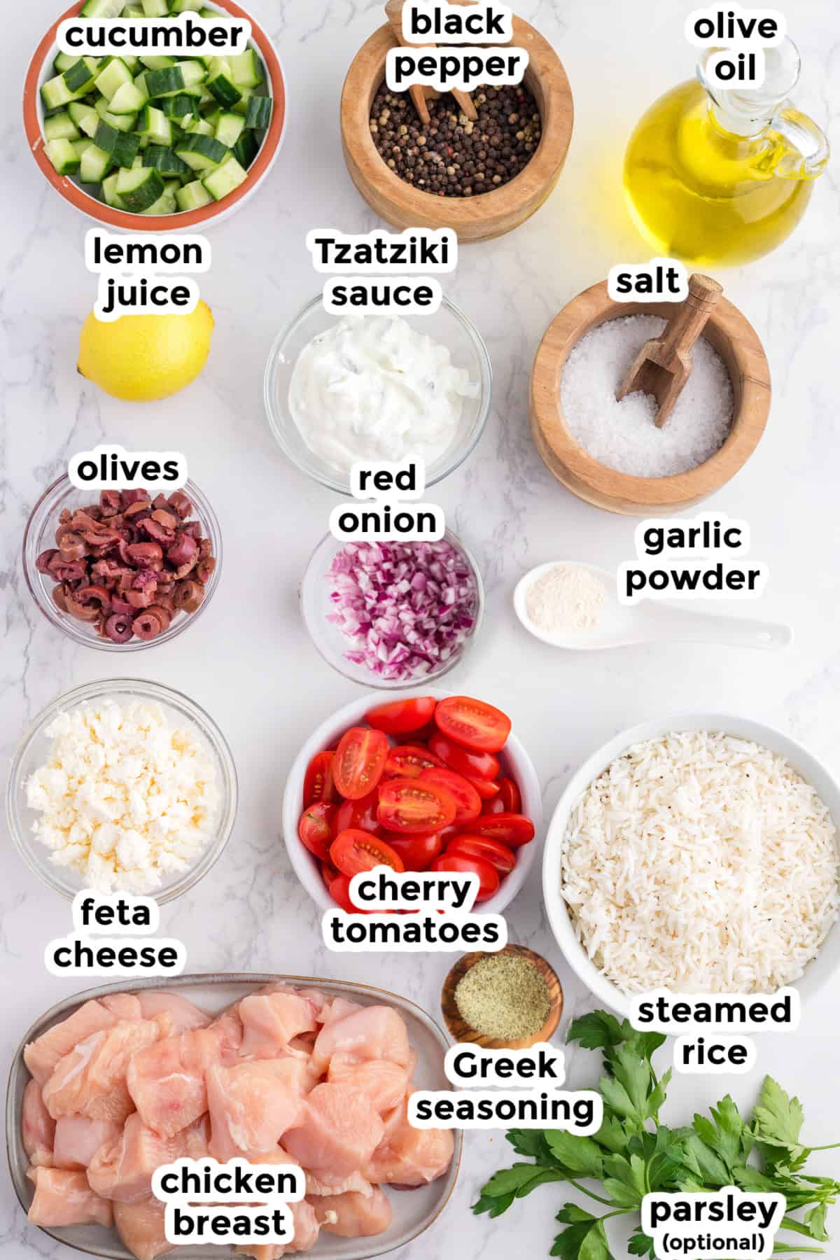 Ingredients for a Greek chicken rice bowl are arranged on a counter with text labels.