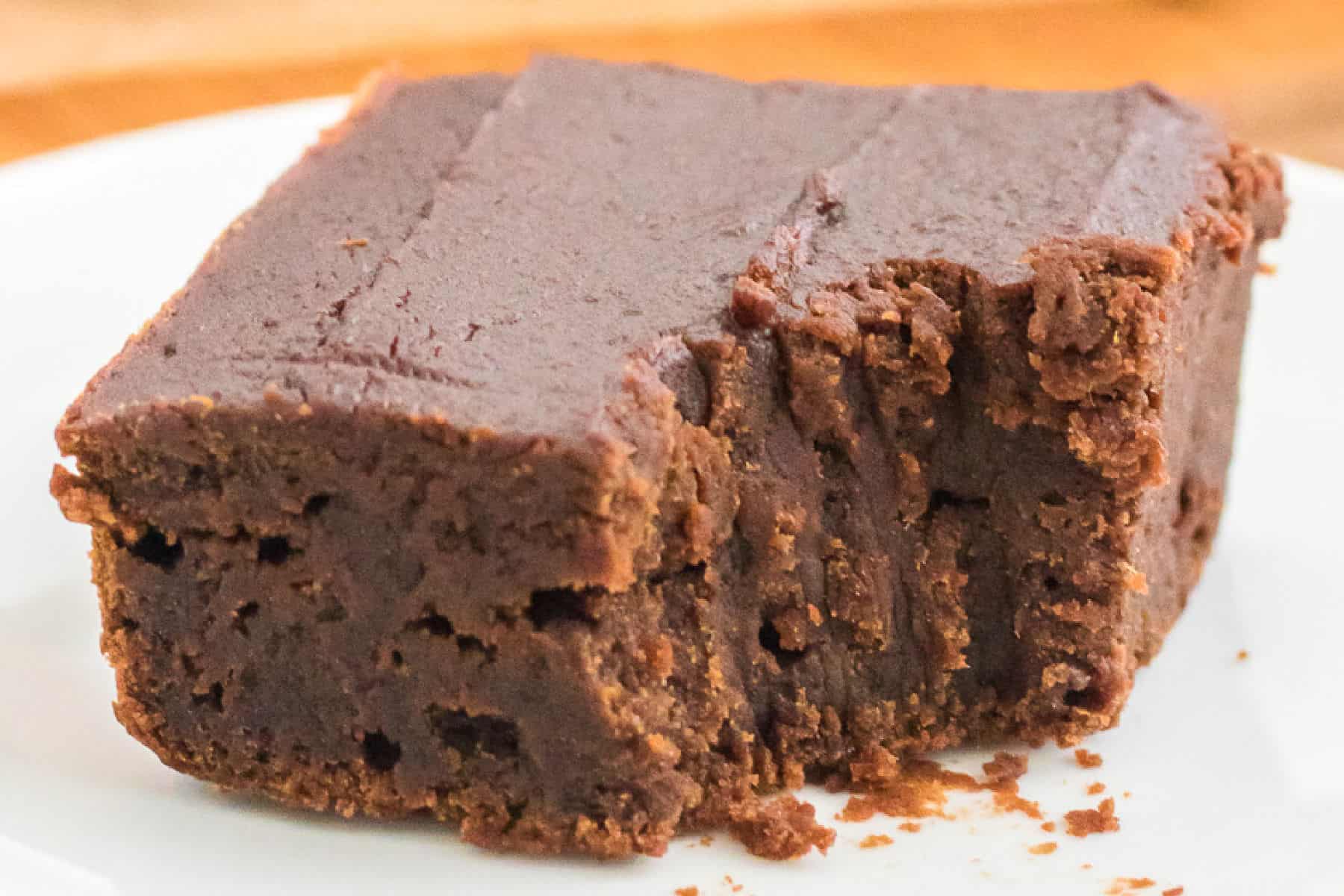 A thick, square piece of chocolate pumpkin brownies with a bite taken out of one side, resting on a white plate.