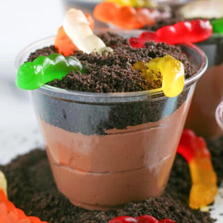 A plastic cup filled with chocolate pudding, topped with crushed cookies and several colorful gummy worms for chocolate dirt cups.