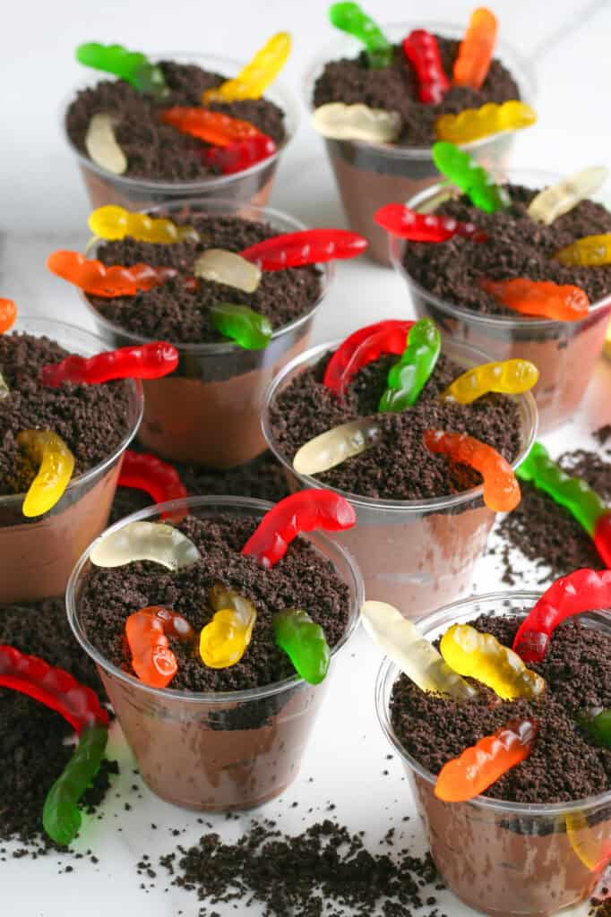 Plastic cups filled with chocolate pudding, crushed chocolate cookies resembling dirt, and topped with colorful gummy worms make classic chocolate dirt cups.
