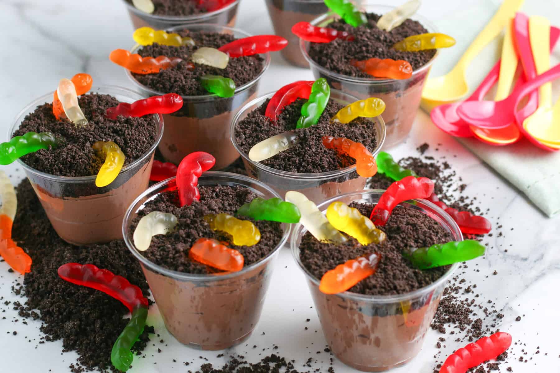 Clear plastic cups filled with chocolate pudding, crushed cookies, and gummy worms cto make chocolate dirt cups.