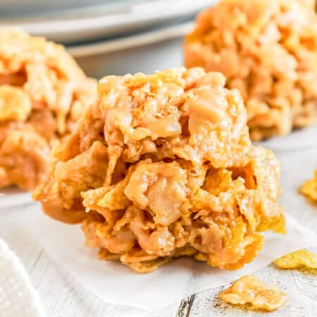 A close-up of a no-bake cornflake cookie on a piece of parchment paper with two more cookies in the background.