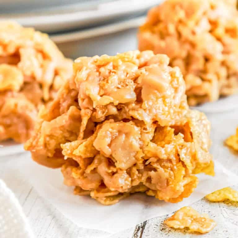 A close-up of a no-bake cornflake cookie on a piece of parchment paper with two more cookies in the background.