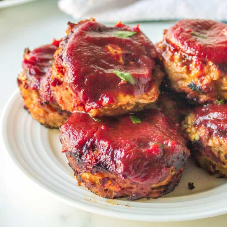 A white plate holds several mini ground turkey meatloaf muffins topped with a bbq sauce.
