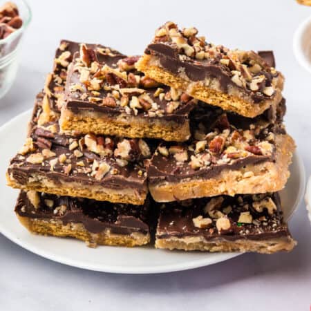 A stack of chocolate-topped graham cracker toffee bars sprinkled with chopped pecans on a white plate.