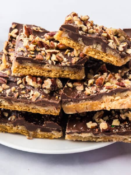A stack of chocolate-topped graham cracker toffee bars sprinkled with chopped pecans on a white plate.